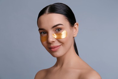 Beautiful young woman with under eye patches on grey background