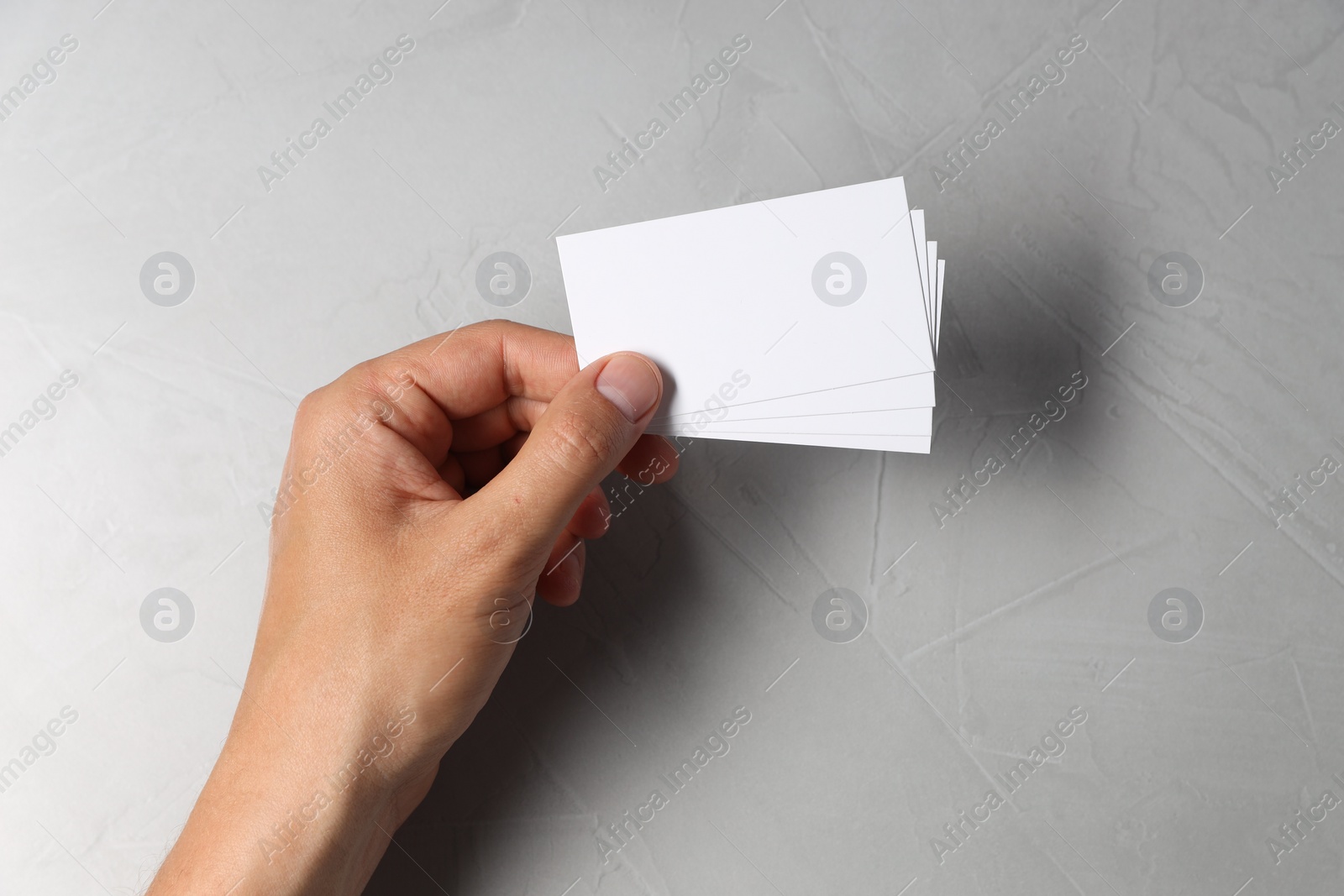 Photo of Man holding white blank cards at light grey table, top view. Mockup for design