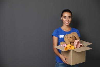 Female volunteer holding box with donations on grey background. Space for text