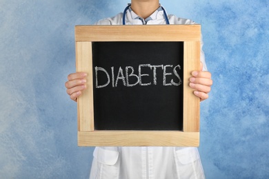 Photo of Doctor holding chalkboard with word DIABETES on color background