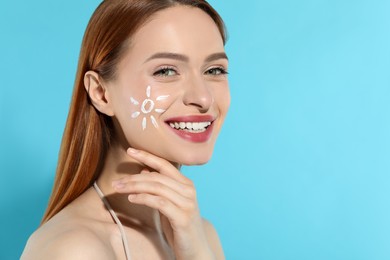 Photo of Beautiful young woman with sun protection cream on her face against light blue background, space for text
