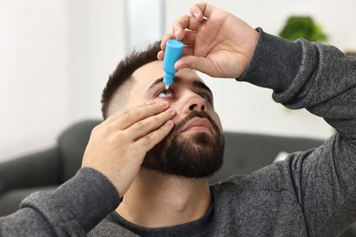 Photo of Young man applying medical eye drops indoors, closeup