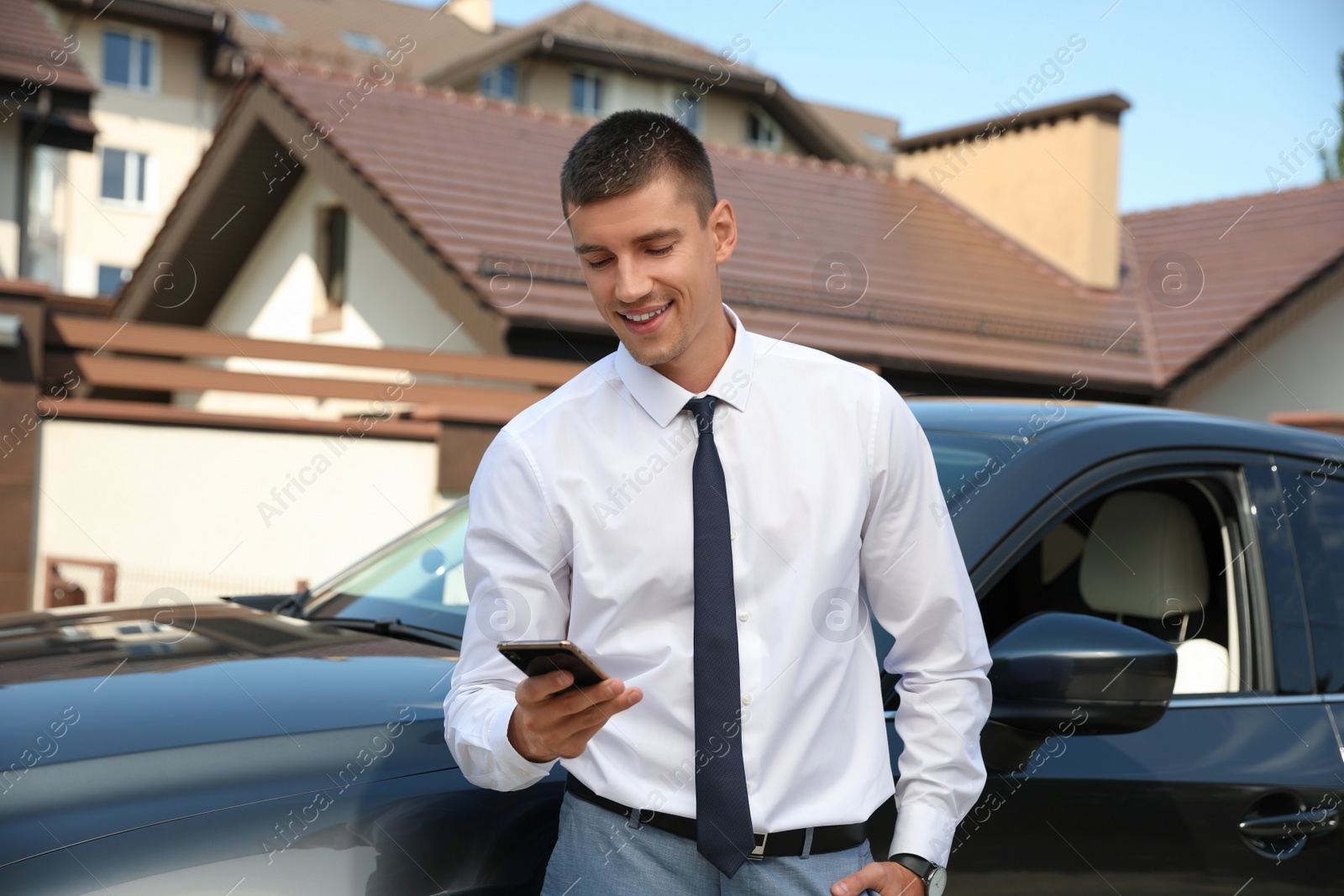 Photo of Attractive young man with smartphone near luxury car outdoors