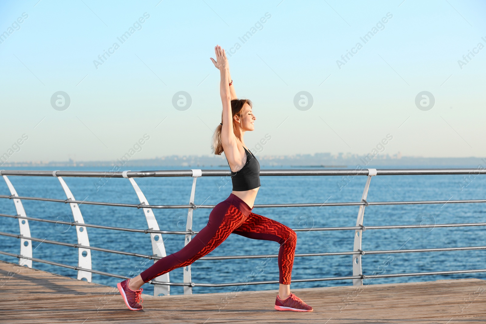 Photo of Young woman doing fitness exercises on pier in morning