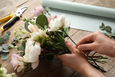 Photo of Florist creating beautiful bouquet at wooden table, closeup