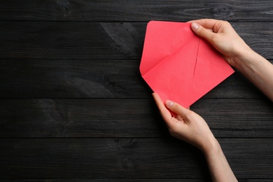 Woman holding red paper envelope on black wooden background, closeup. Space for text