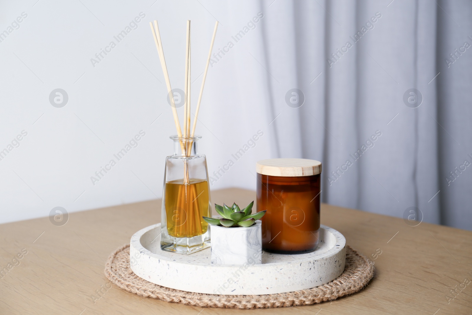 Photo of Beautiful plant, candle and aromatic reed air freshener on wooden table indoors. Interior elements