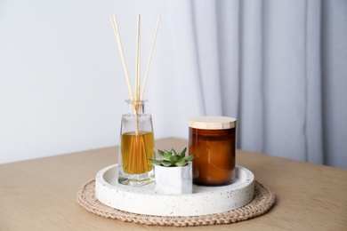 Beautiful plant, candle and aromatic reed air freshener on wooden table indoors. Interior elements