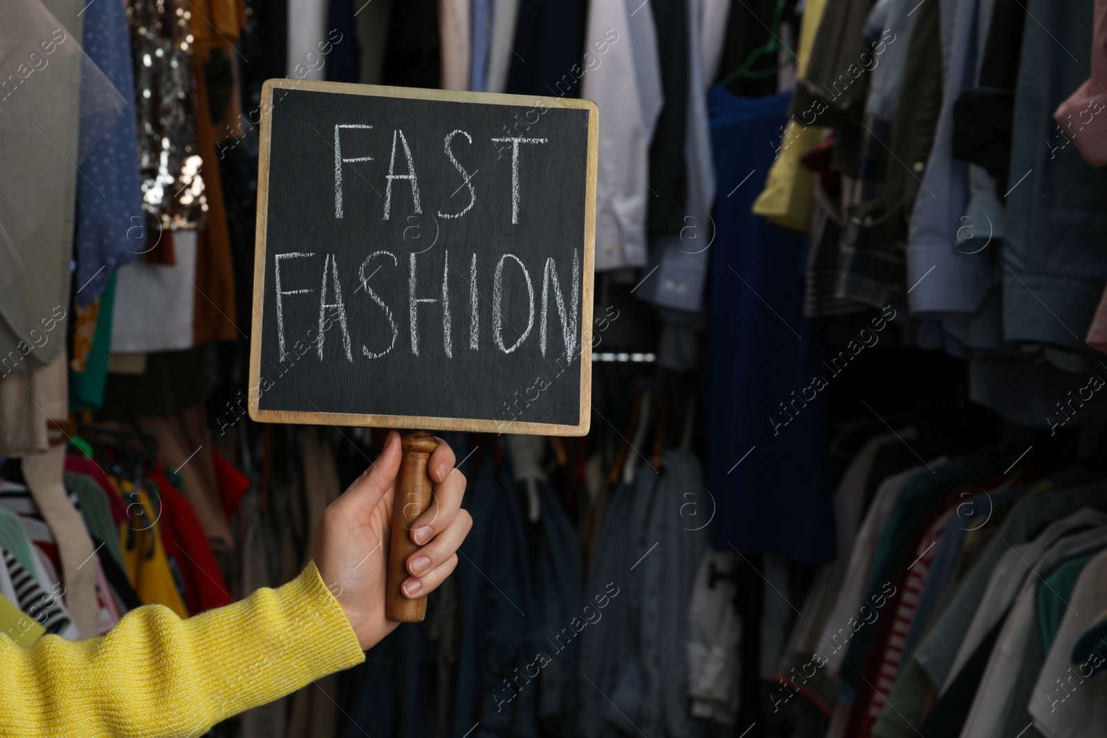 Photo of Woman holding small chalkboard with phrase FAST FASHION in clothes store, closeup. Space for text