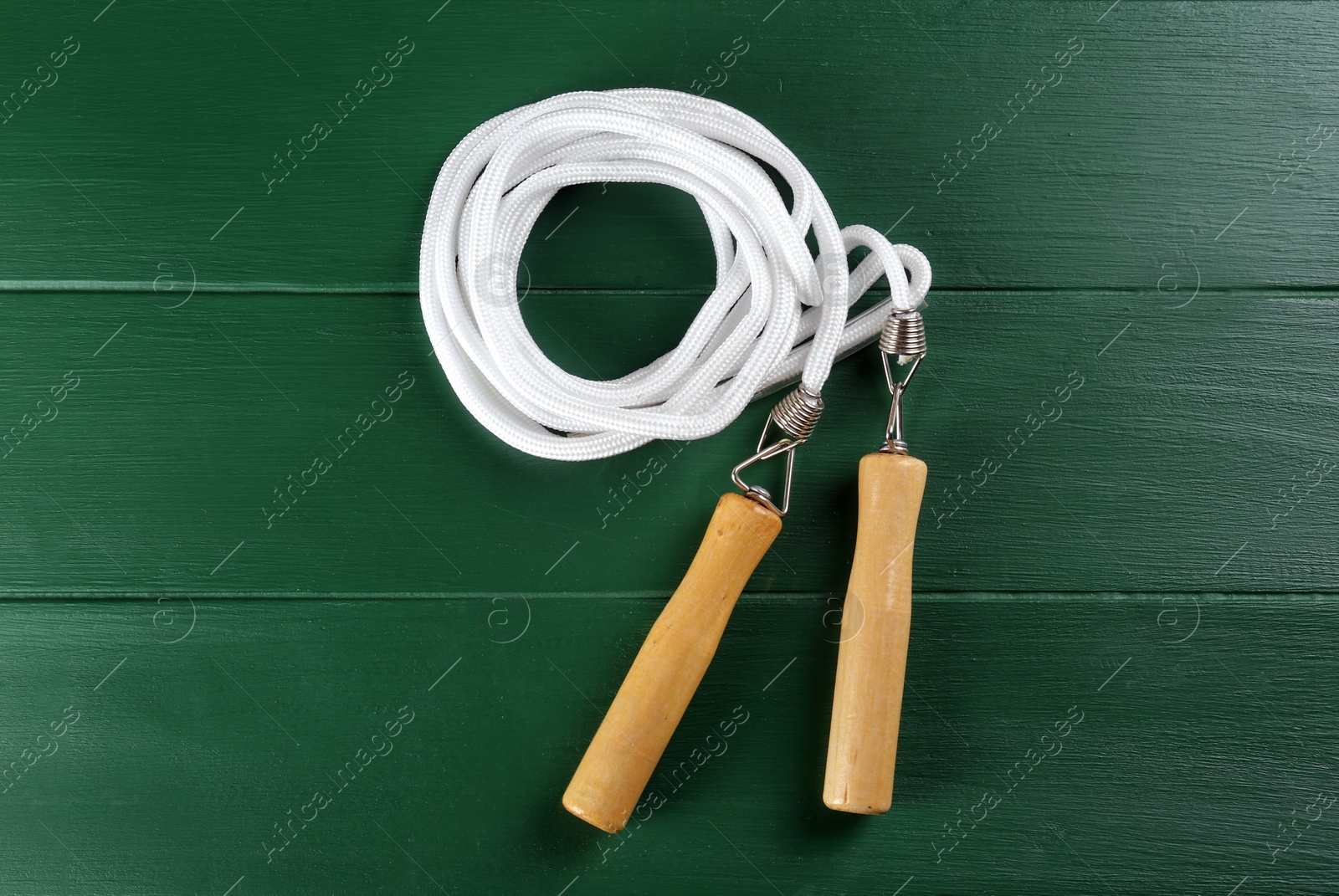 Photo of Skipping rope on green wooden table, top view. Sports equipment