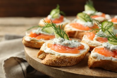 Photo of Tasty canapes with salmon, cucumber, cream cheese and dill on wooden stand, closeup
