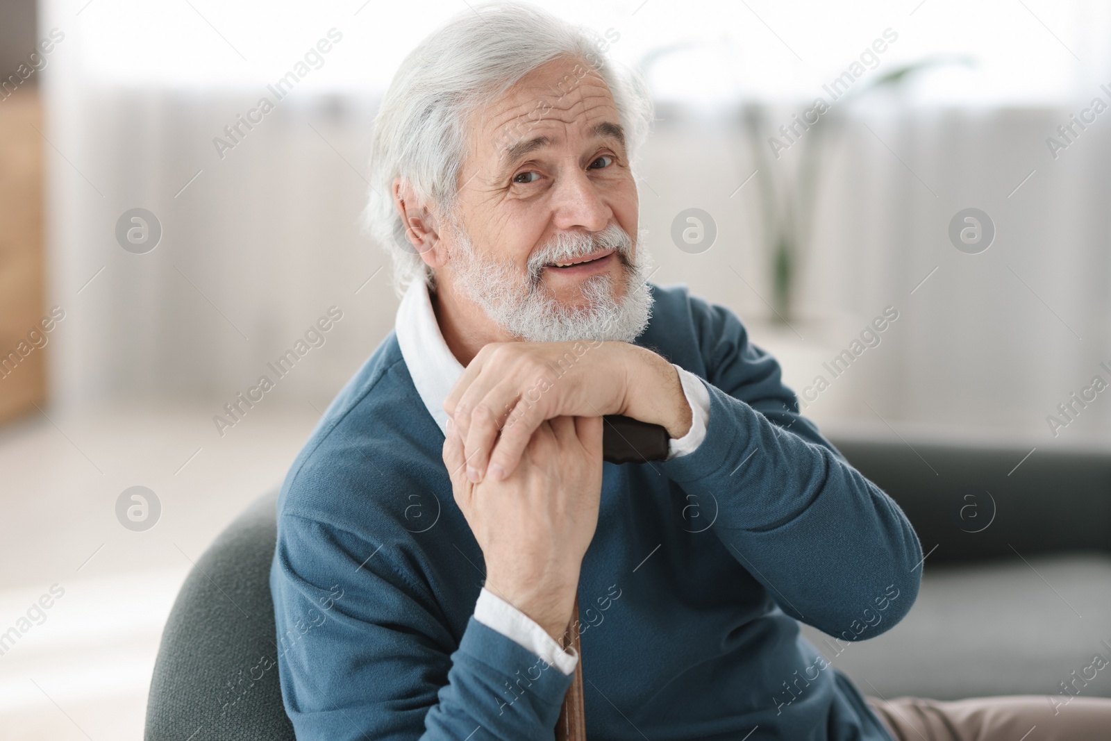 Photo of Portrait of happy grandpa with walking cane sitting on sofa indoors