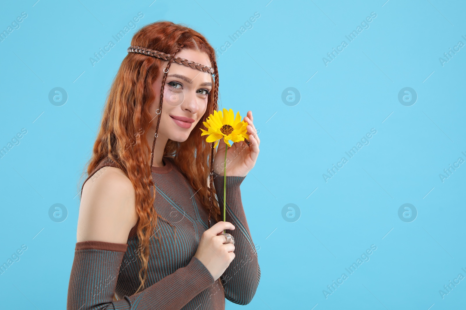 Photo of Beautiful young hippie woman with sunflower on light blue background, space for text