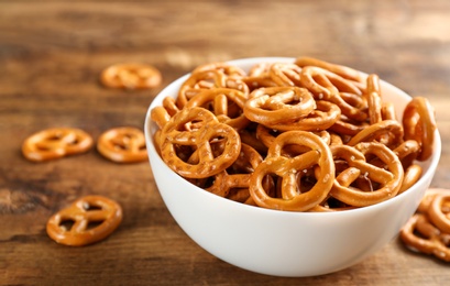 Photo of Bowl with delicious pretzel crackers on wooden table, closeup