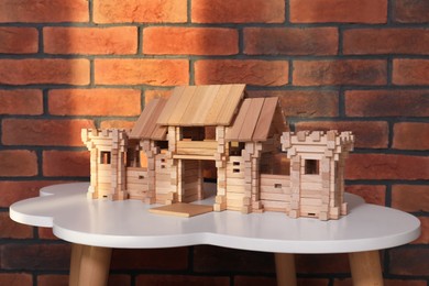 Photo of Wooden castle on white table near brick wall. Children's toy