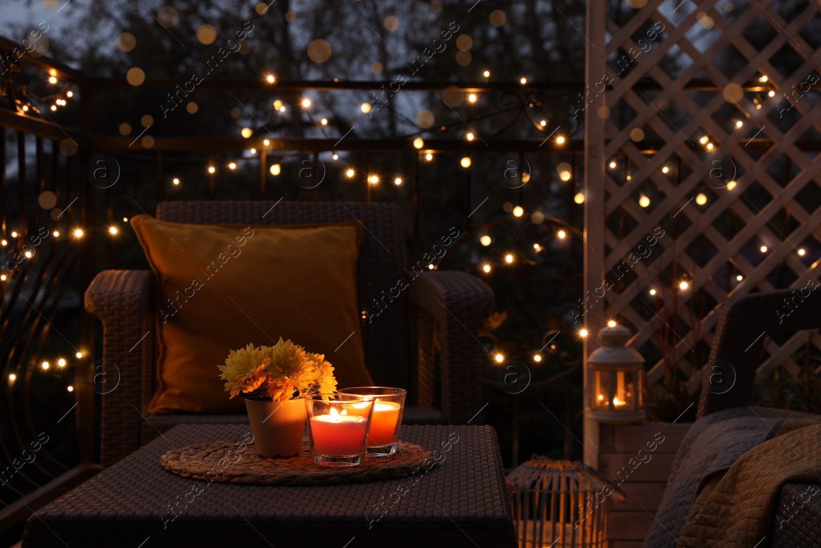 Photo of Beautiful view of garden furniture with pillow, soft blanket and burning candles at balcony