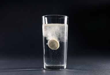 Photo of Effervescent pill dissolving in glass of water on grey table