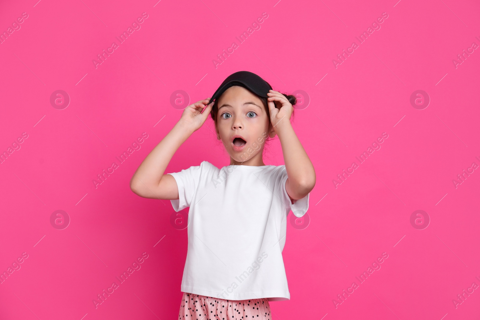 Photo of Cute girl in pajamas with sleep mask on pink background