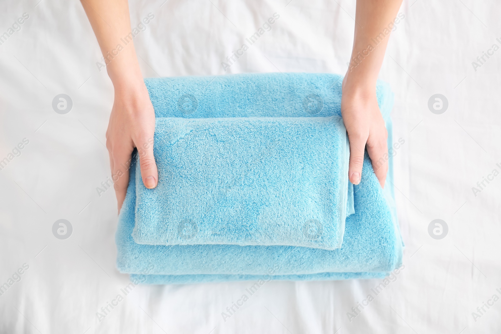 Photo of Woman folding clean towels on bed, closeup