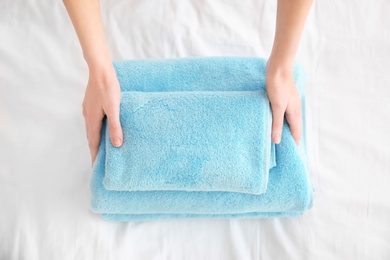 Photo of Woman folding clean towels on bed, closeup