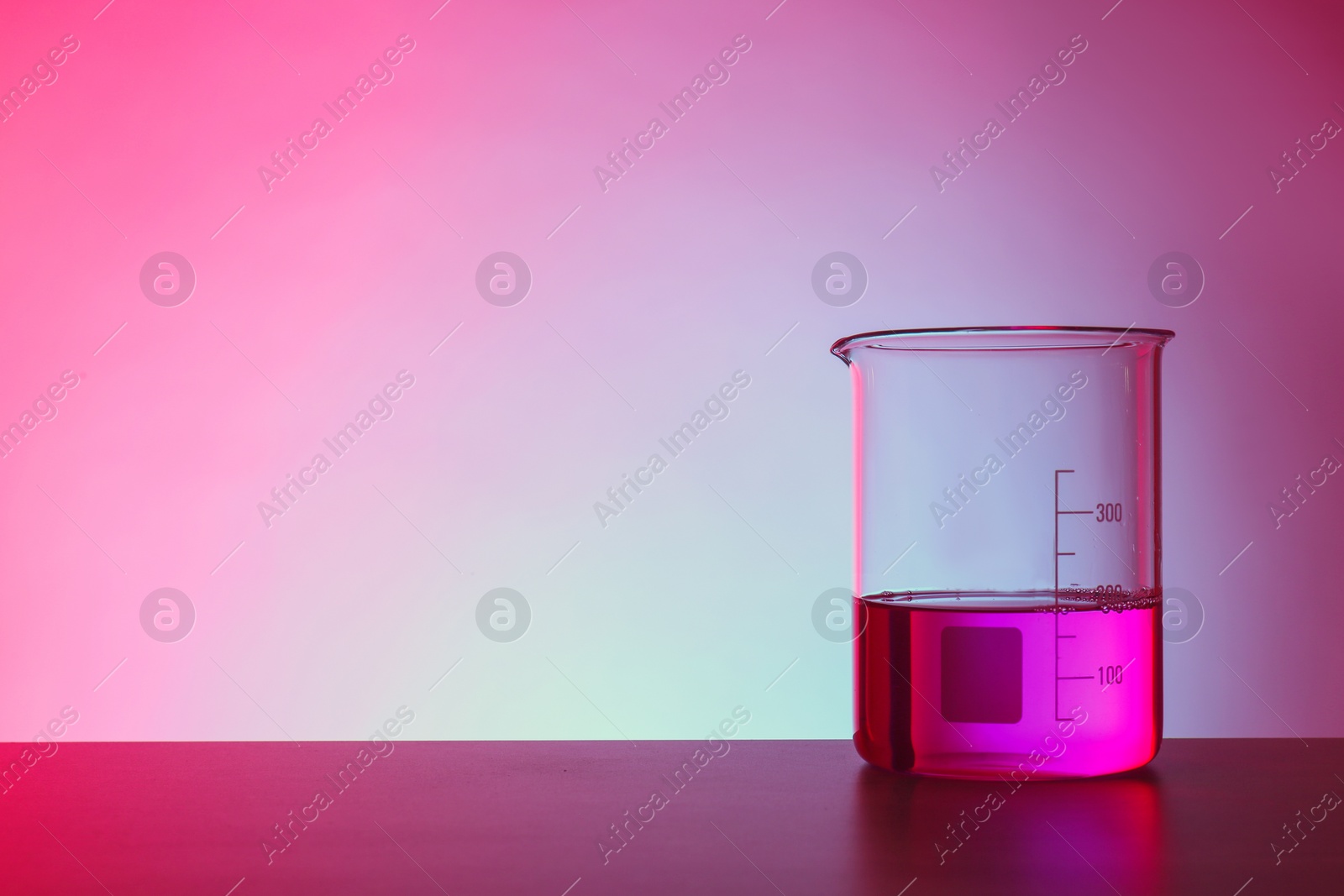 Photo of Beaker with liquid on table against color background. Chemistry laboratory glassware