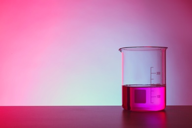 Photo of Beaker with liquid on table against color background. Chemistry laboratory glassware