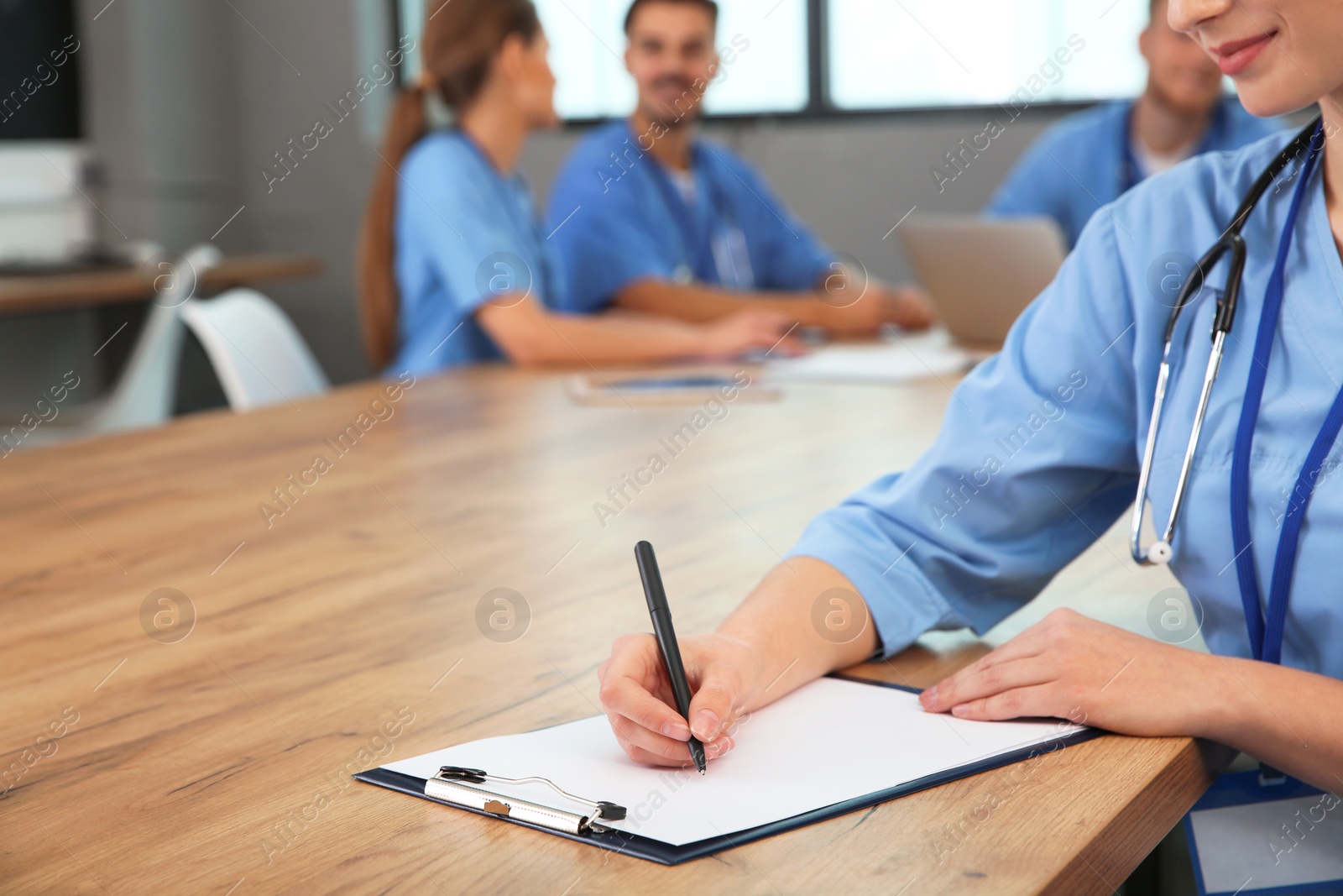 Photo of Medical student with clipboard and her groupmates studying in university library, closeup