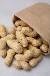 Photo of Paper bag with fresh unpeeled peanuts on grey table, closeup