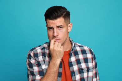 Photo of Man biting his nails on light blue background. Bad habit