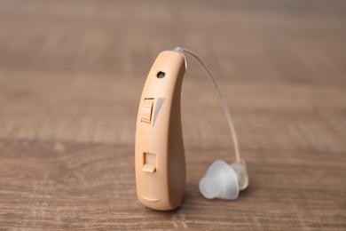 Photo of Hearing aid on wooden table, closeup. Medical device