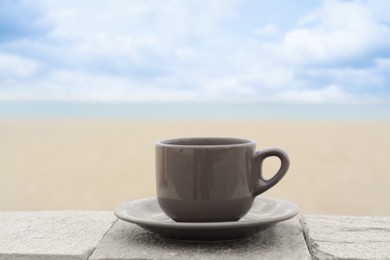 Photo of Ceramic cup of hot drink on stone surface near sea