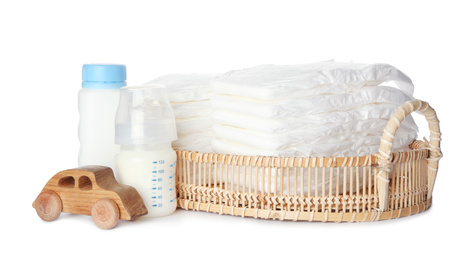Photo of Wicker tray with disposable diapers, toy car and bottles on white background
