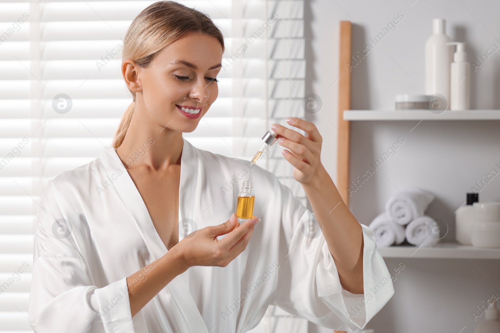 Photo of Beautiful woman with cosmetic serum in her hands in bathroom
