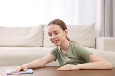 Woman with microfiber cloth cleaning wooden table in room