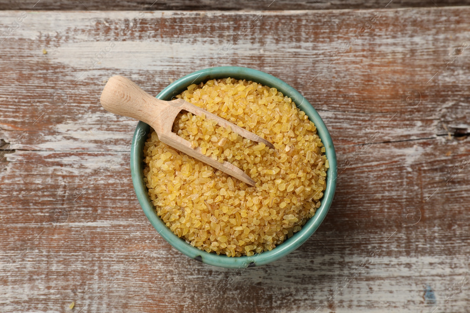 Photo of Bowl and scoop with raw bulgur on wooden table, top view