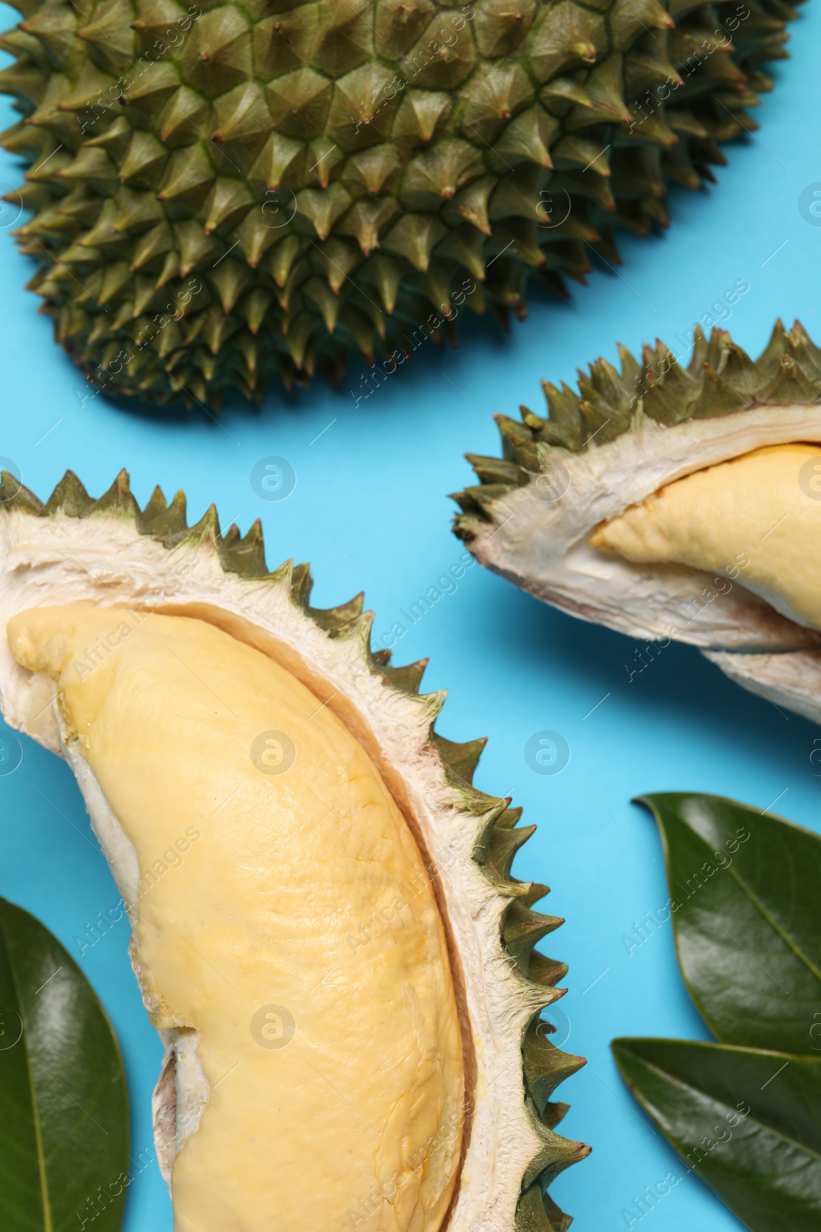 Photo of Fresh ripe durians and leaves on light blue background, flat lay