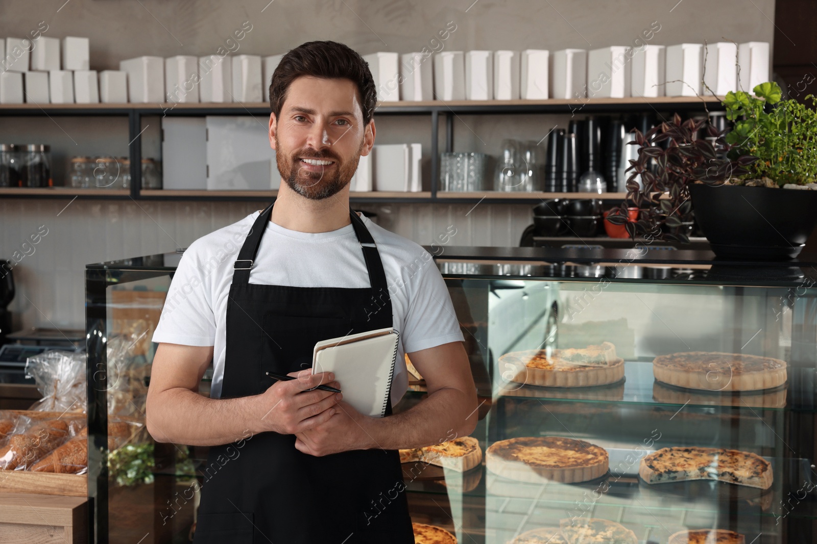 Photo of Happy seller with notebook and pen near showcase in bakery shop