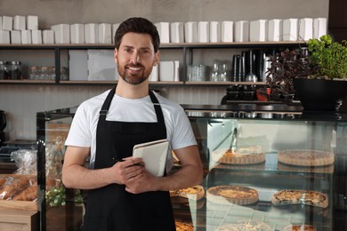 Photo of Happy seller with notebook and pen near showcase in bakery shop