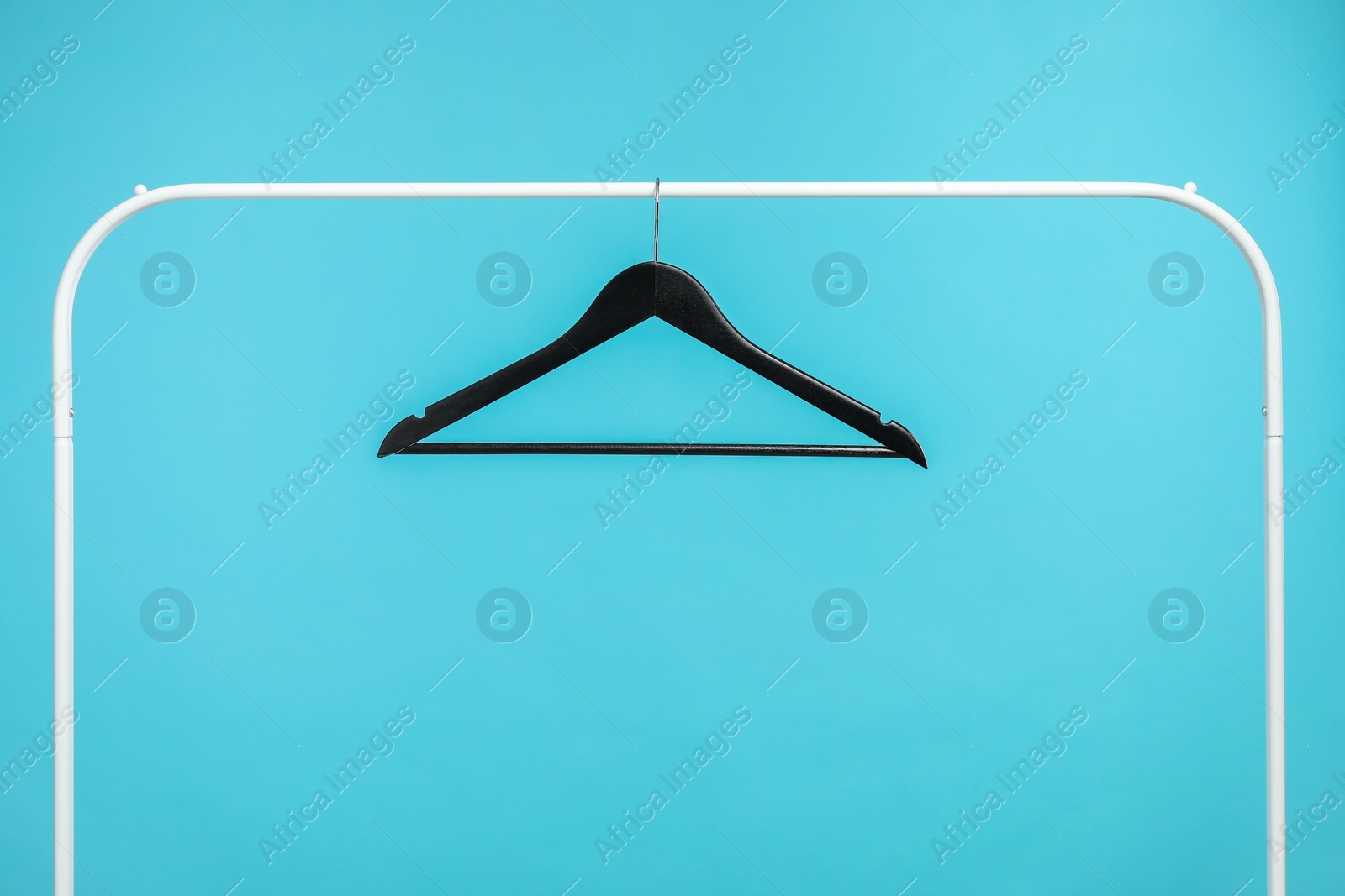 Photo of Black clothes hanger on rack against light blue background