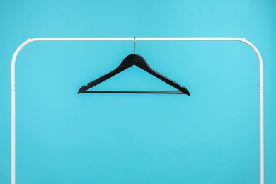 Photo of Black clothes hanger on rack against light blue background