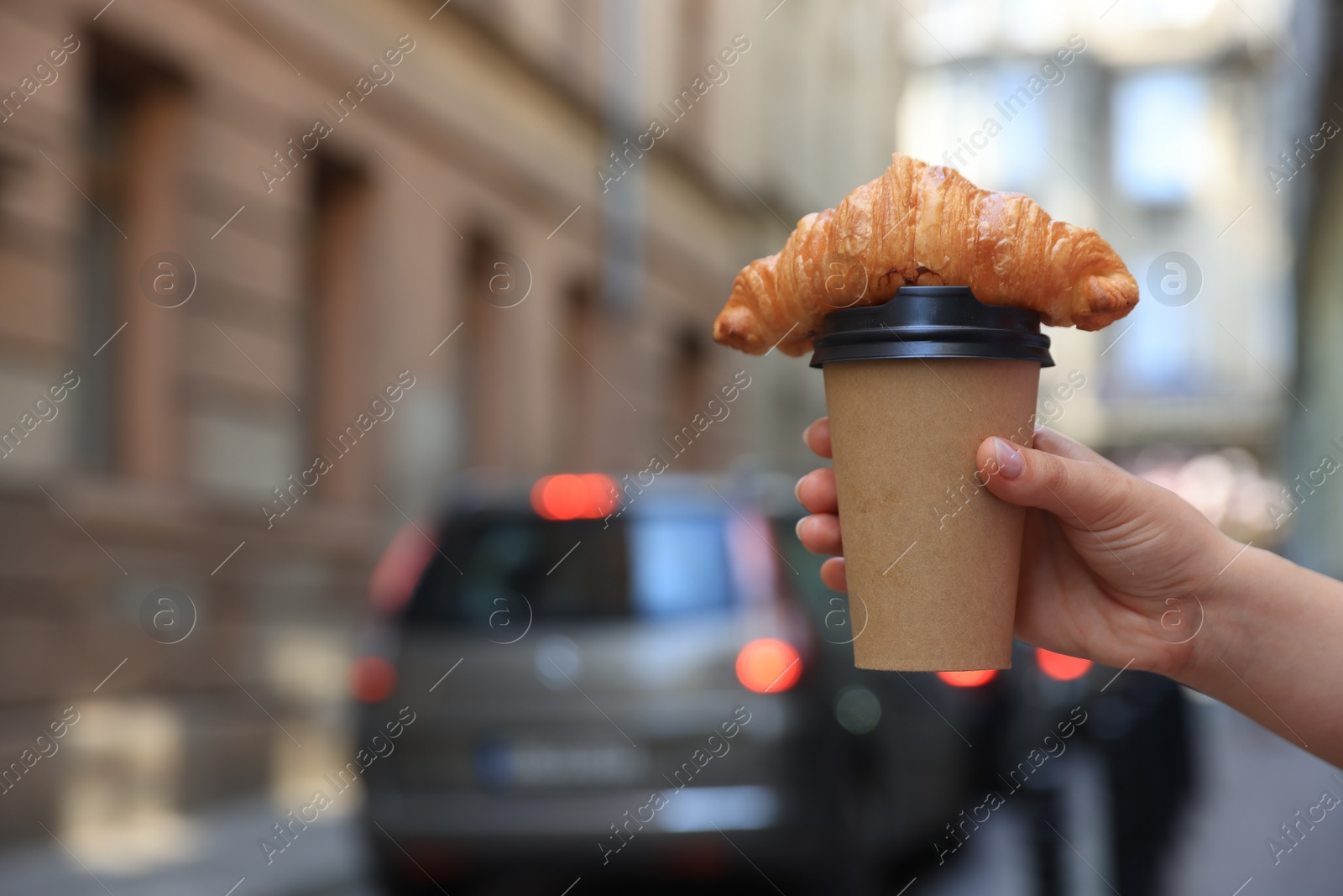 Photo of Woman holding tasty croissant and cup of coffee on city street, closeup. Space for text