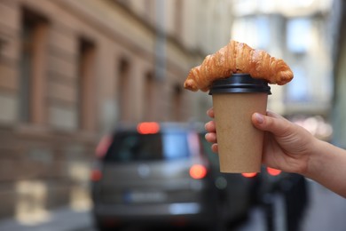 Woman holding tasty croissant and cup of coffee on city street, closeup. Space for text