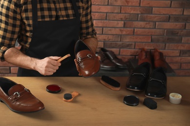 Photo of Craftsman taking professional care of brown leather shoes in workshop, closeup