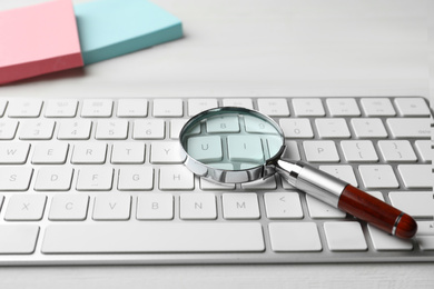 Photo of Magnifier glass and keyboard on white table, closeup. Find keywords concept