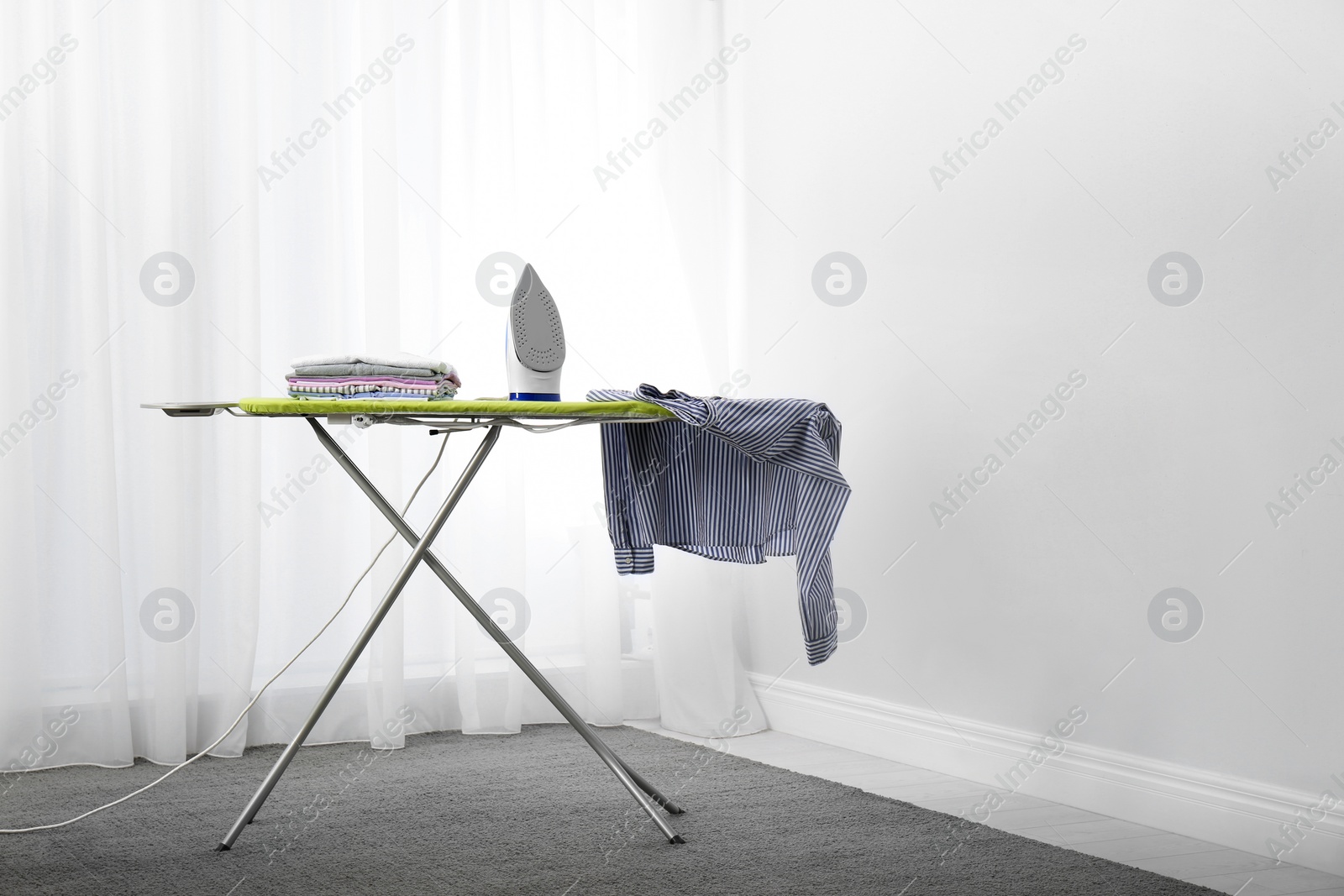 Photo of Modern electric iron and clothes on board  indoors, space for text. Laundry day