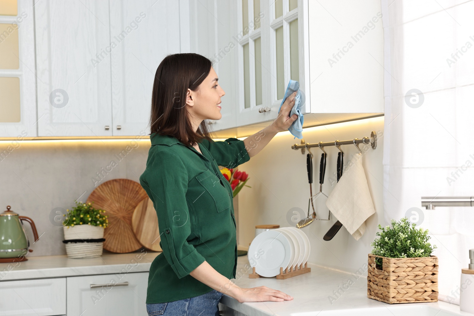 Photo of Woman cleaning furniture with rag in kitchen