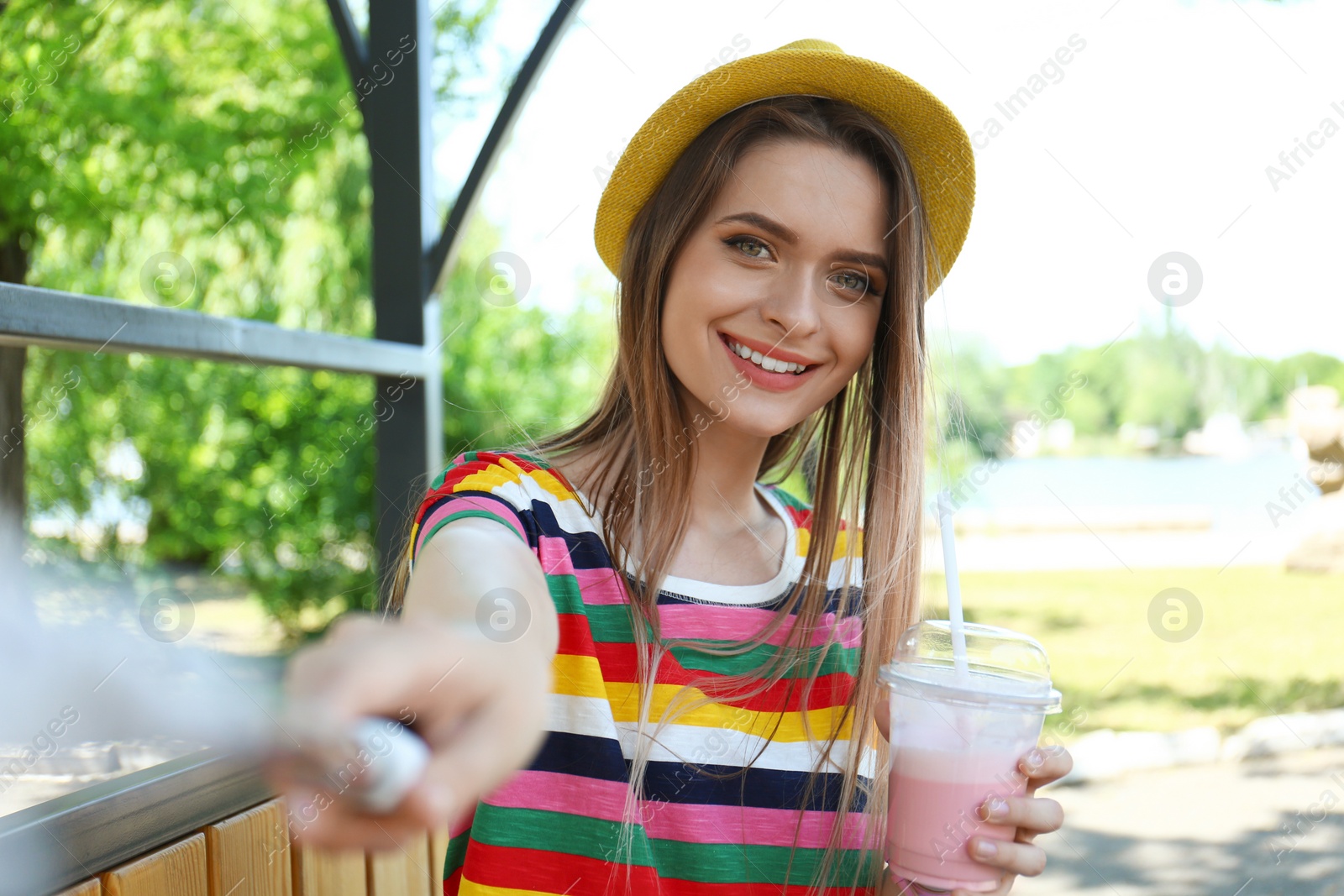 Photo of Happy young woman with drink taking selfie in park