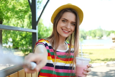 Happy young woman with drink taking selfie in park