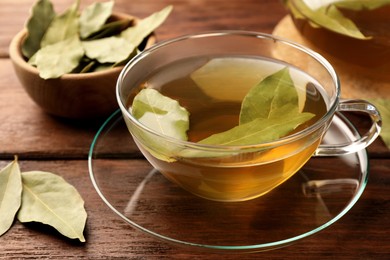 Photo of Cup of freshly brewed tea with bay leaves on wooden table, closeup