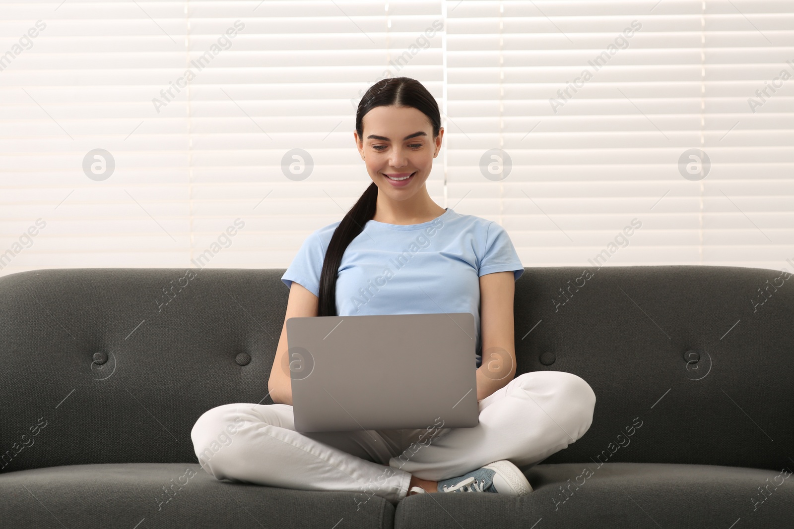 Photo of Happy woman working with laptop on sofa indoors